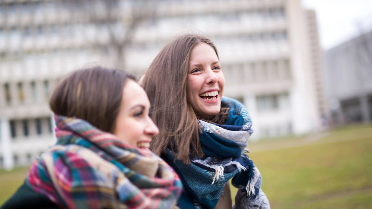 Zwei junge lachende Frauen auf dem Campus.